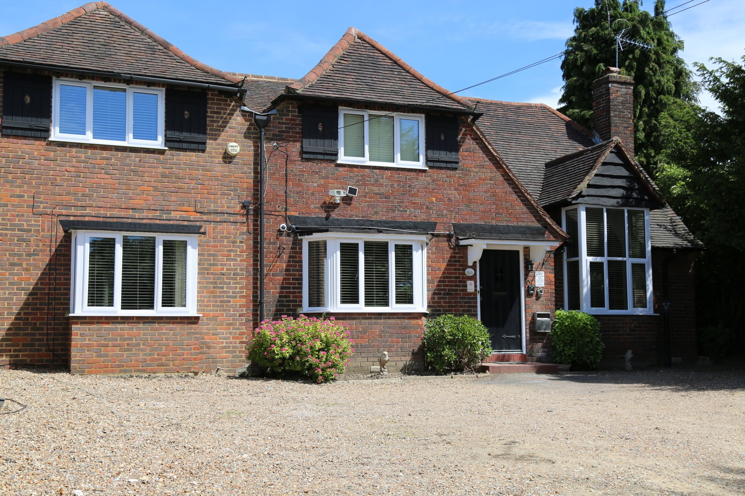 A two-story brick house with a front porch, a chimney, and a small garden area.