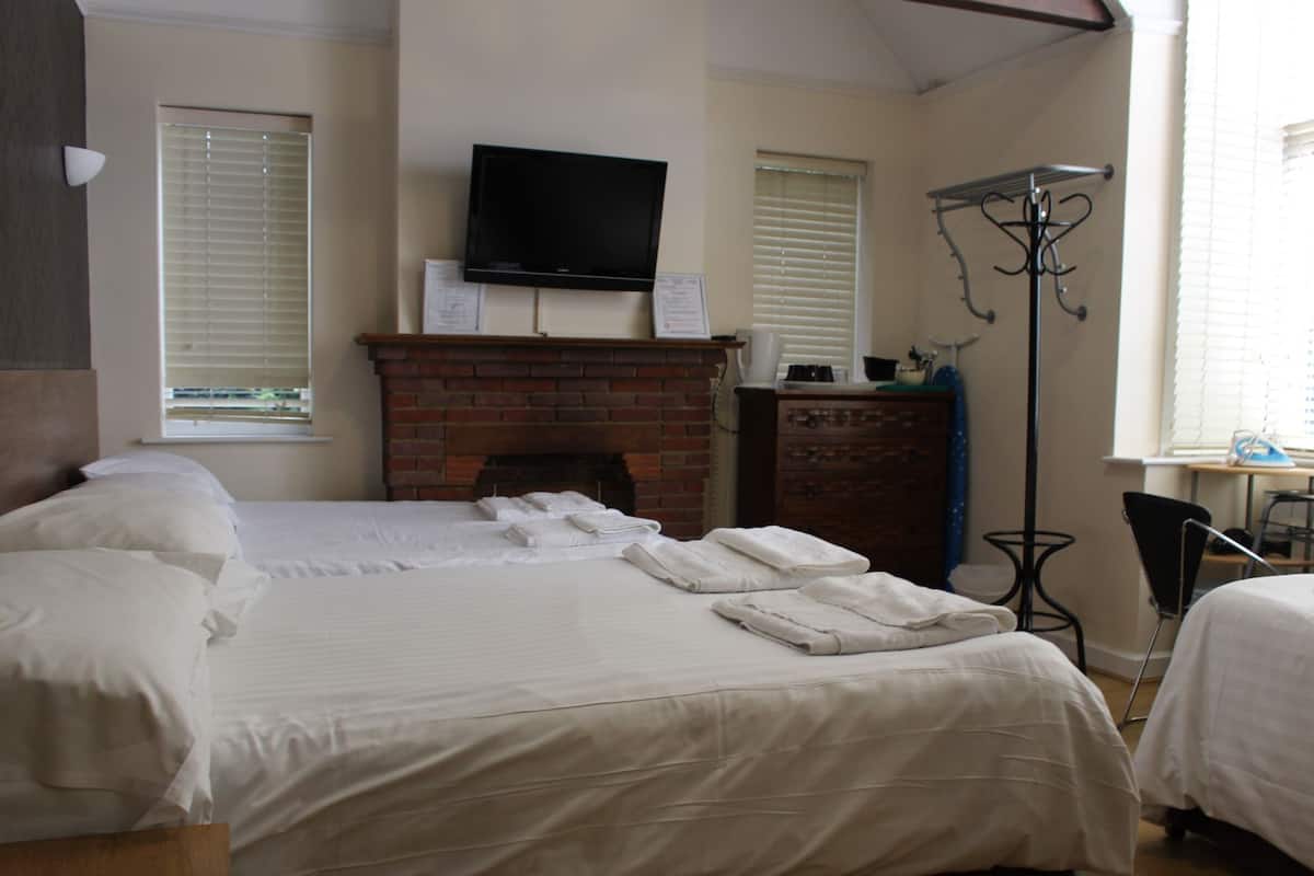 A hotel room with two beds, a flat-screen TV mounted above a brick fireplace, and a coat rack by the window.