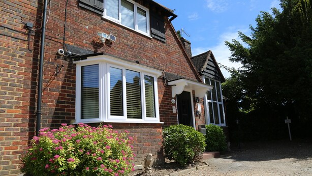 A two-story brick house with a white-framed window, a small porch, and a gravel driveway. - Debden Guest House (Uxbridge)