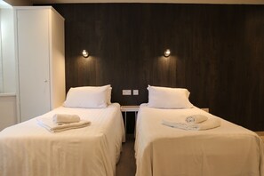 A hotel room with two single beds, a small table, and a wardrobe.