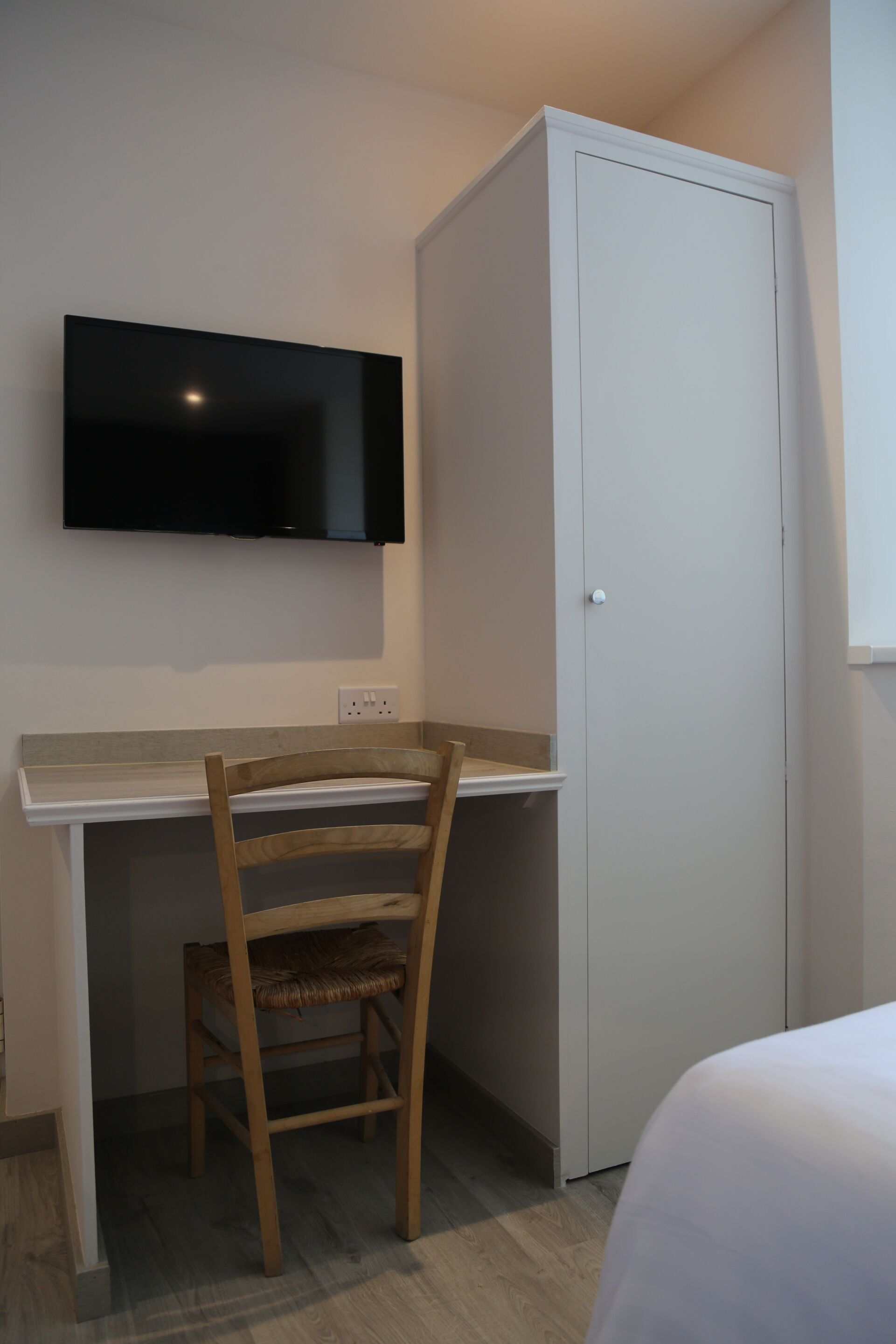 Un dormitorio con cama, escritorio con silla, televisor montado en la pared y armario.