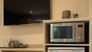 A kitchenette with a microwave, a small refrigerator, a chair, and a flat-screen TV mounted on the wall. - Debden Guest House (Uxbridge)