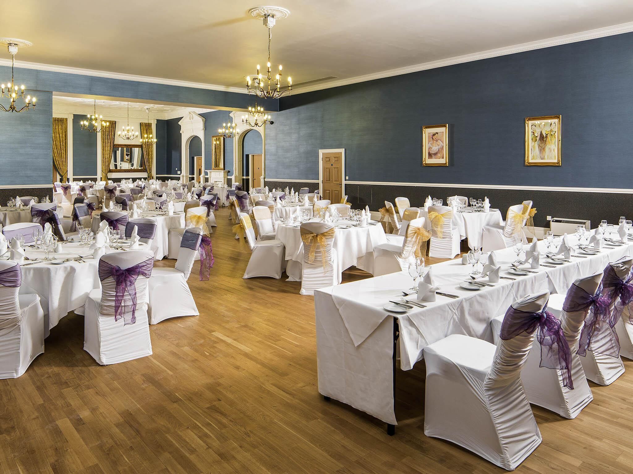 A banquet hall with round tables, white tablecloths, and chairs with purple sashes.