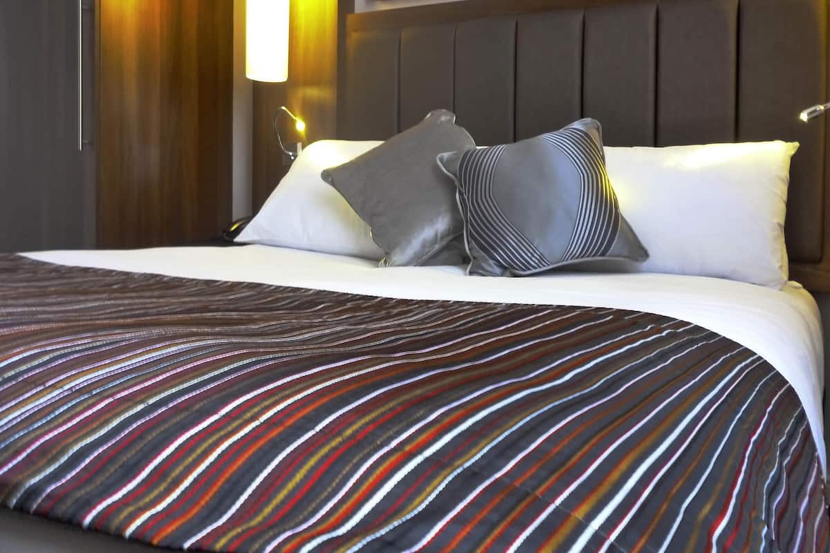 A neatly made bed with striped bedding, a headboard, and a wall-mounted lamp.