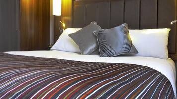 Una cama bien hecha con ropa de cama a rayas, cabecera y lámpara fijada a la pared.