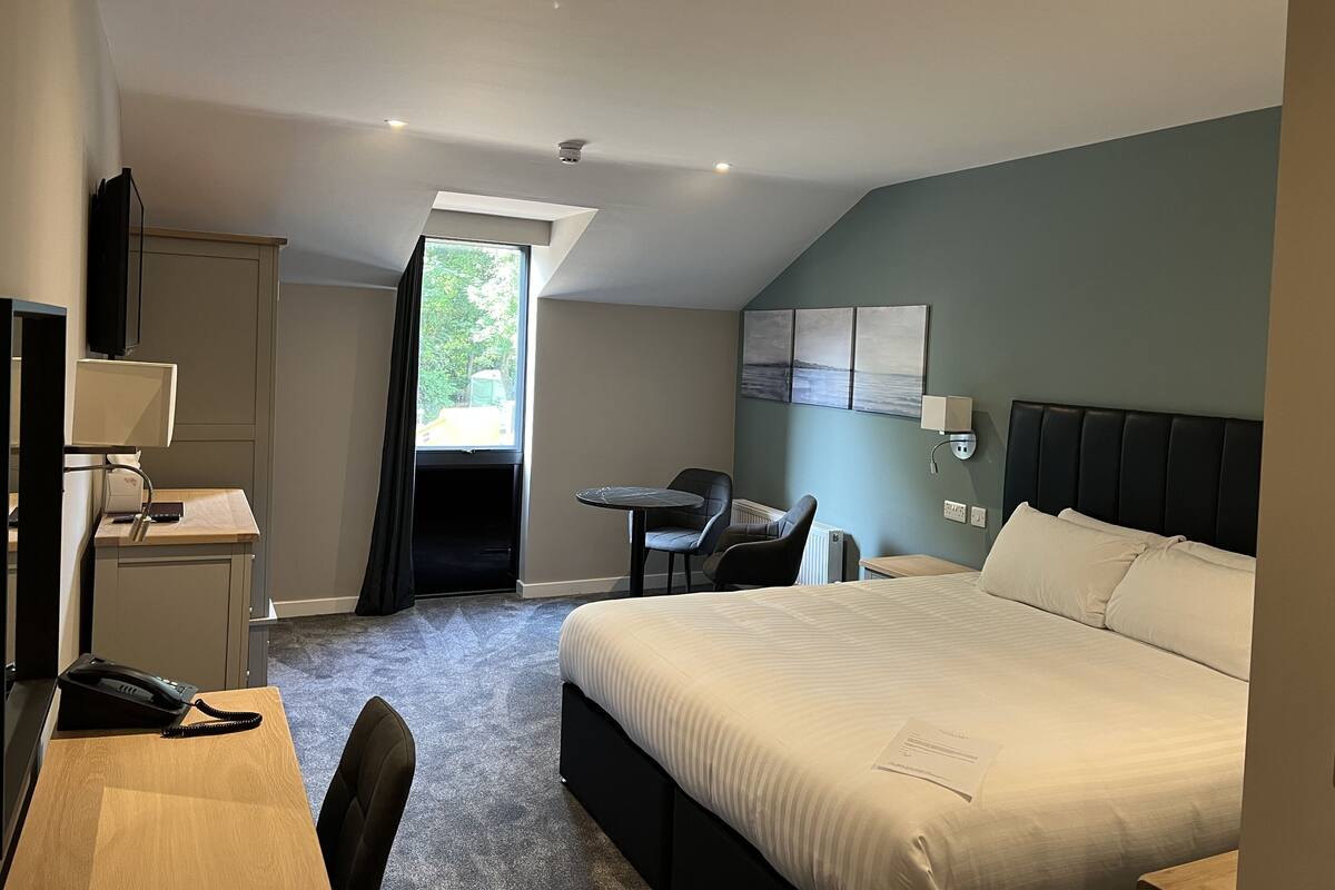 A hotel room with a bed, desk, chair, and a view through a window.