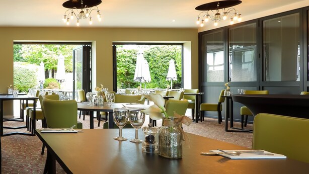 Un ristorante con tavoli apparecchiati per consumare i pasti, ampie finestre con vista all'esterno e lampadari moderni.