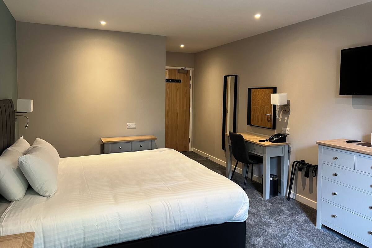 A hotel room with a bed, desk, chair, dresser, and a TV mounted on the wall.