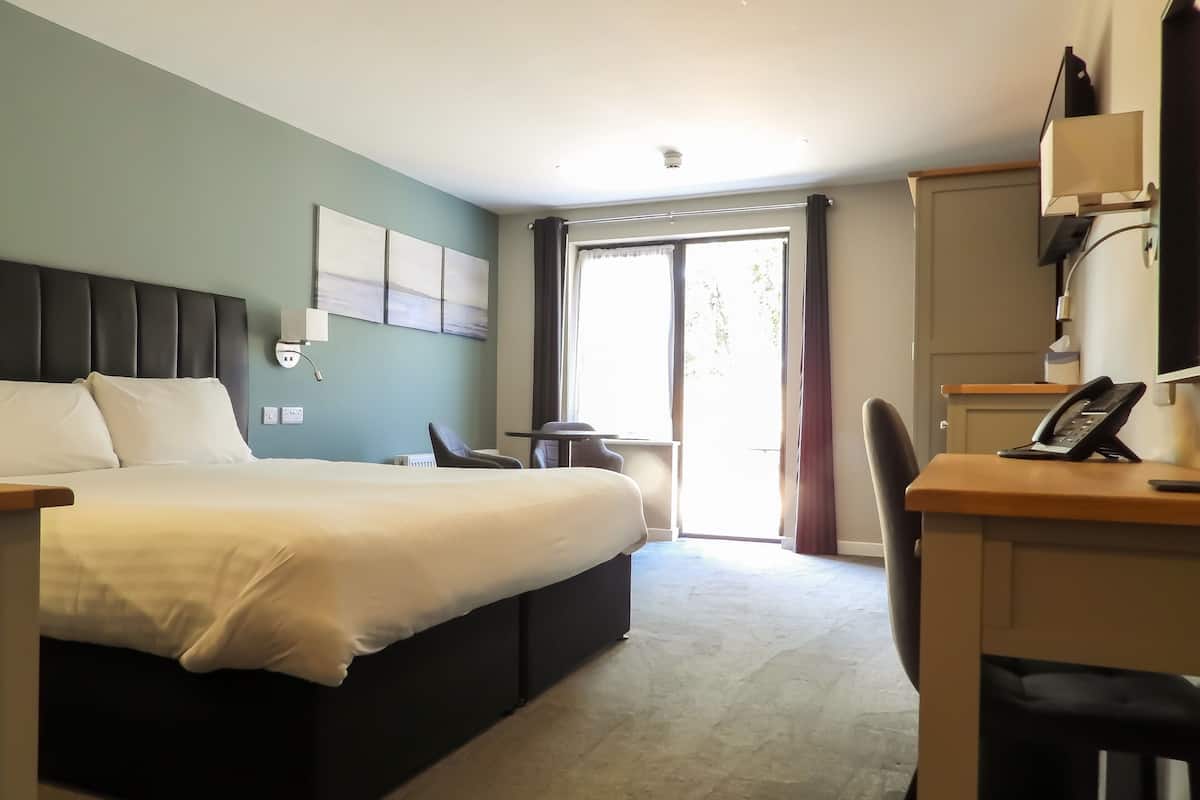 A hotel room with a bed, a desk, a chair, a telephone, and a window with curtains.