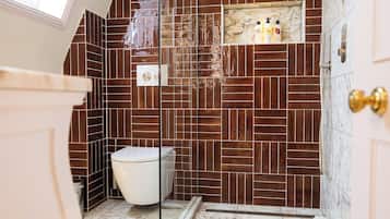 A bathroom with a modern design, featuring a white toilet, a shower area, and a marble-tiled floor.
