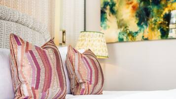 A neatly made bed with striped pillows and a patterned throw, a lamp, and a textured wall with a painting.