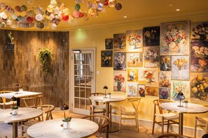 A dining area with round tables, chairs, and a wall adorned with floral paintings. - Dukes Bath (Bath)