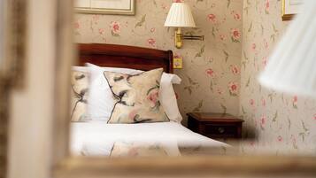A neatly made bed with floral-patterned pillows and a wooden headboard. A bedside table with a lamp and a small drawer is visible.
