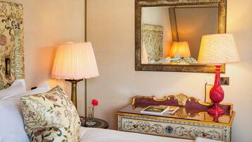 A hotel room with a bed, two bedside lamps, a mirror, a small table with a book, and a decorative chest.