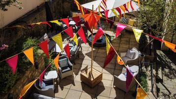 An outdoor patio area with wicker furniture, a stone-tiled floor, and colorful triangular flags.