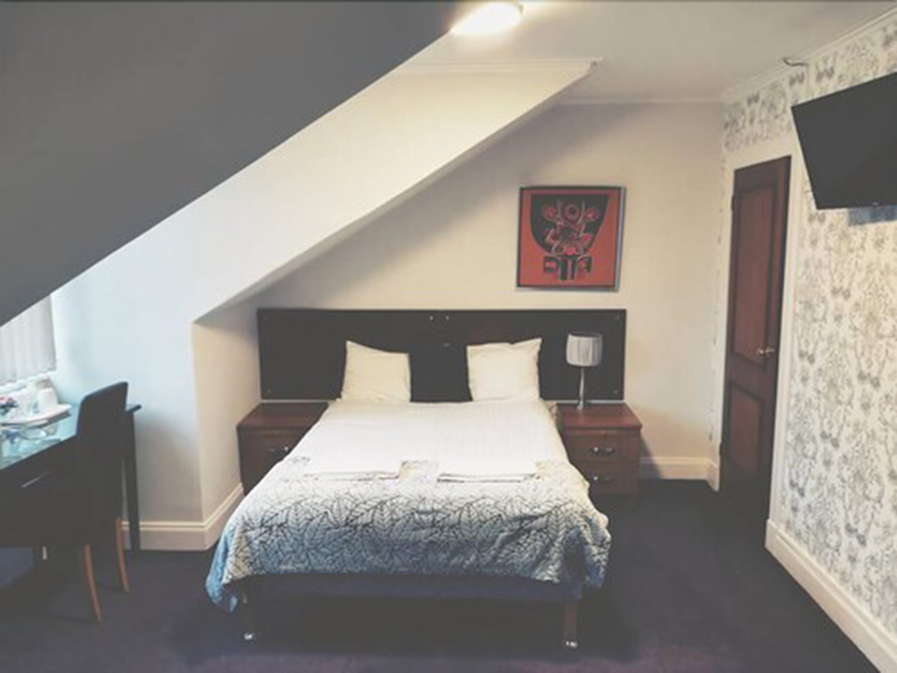A bedroom with a bed, two bedside tables, a desk, and a chair.