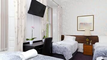 A hotel room with two beds, a desk, a TV, a bedside table, and a window with curtains.