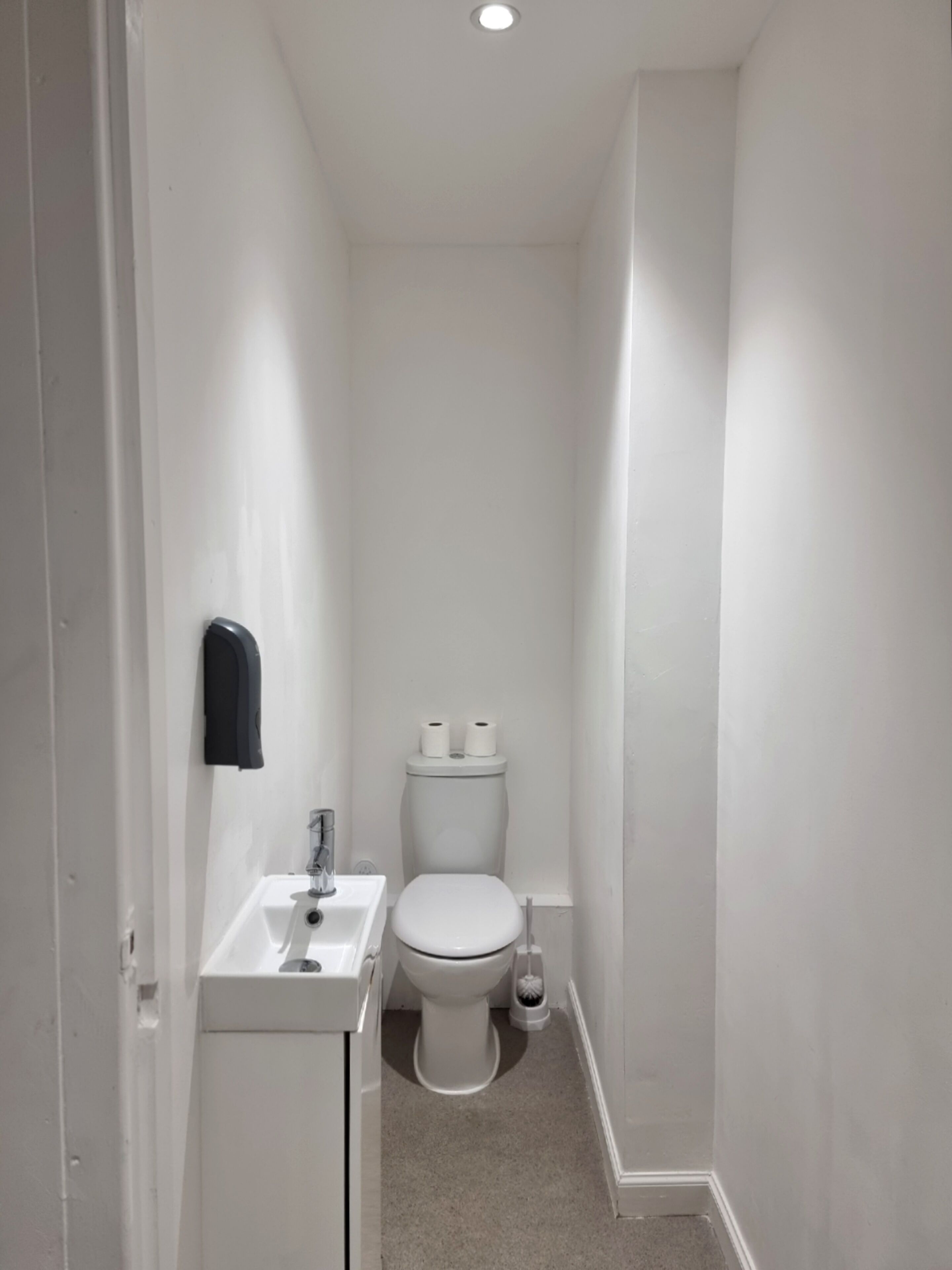 Un baño pequeño y blanco con inodoro, lavamanos y secamanos.