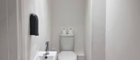 Un baño pequeño y blanco con inodoro, lavamanos y secamanos.