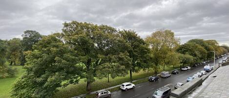 A multi-lane road with parked cars on the side, surrounded by trees and greenery.