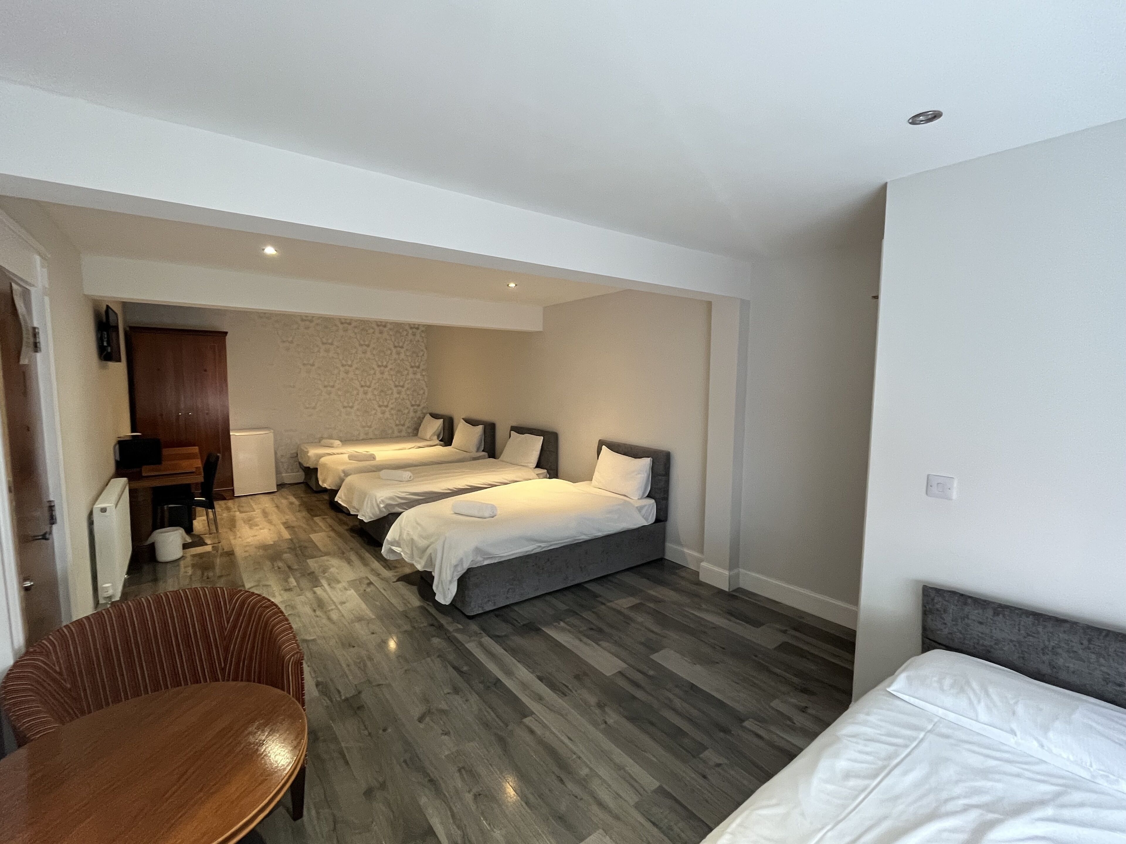Habitación de hotel con tres camas, una mesa de comedor de madera y una kitchenette.