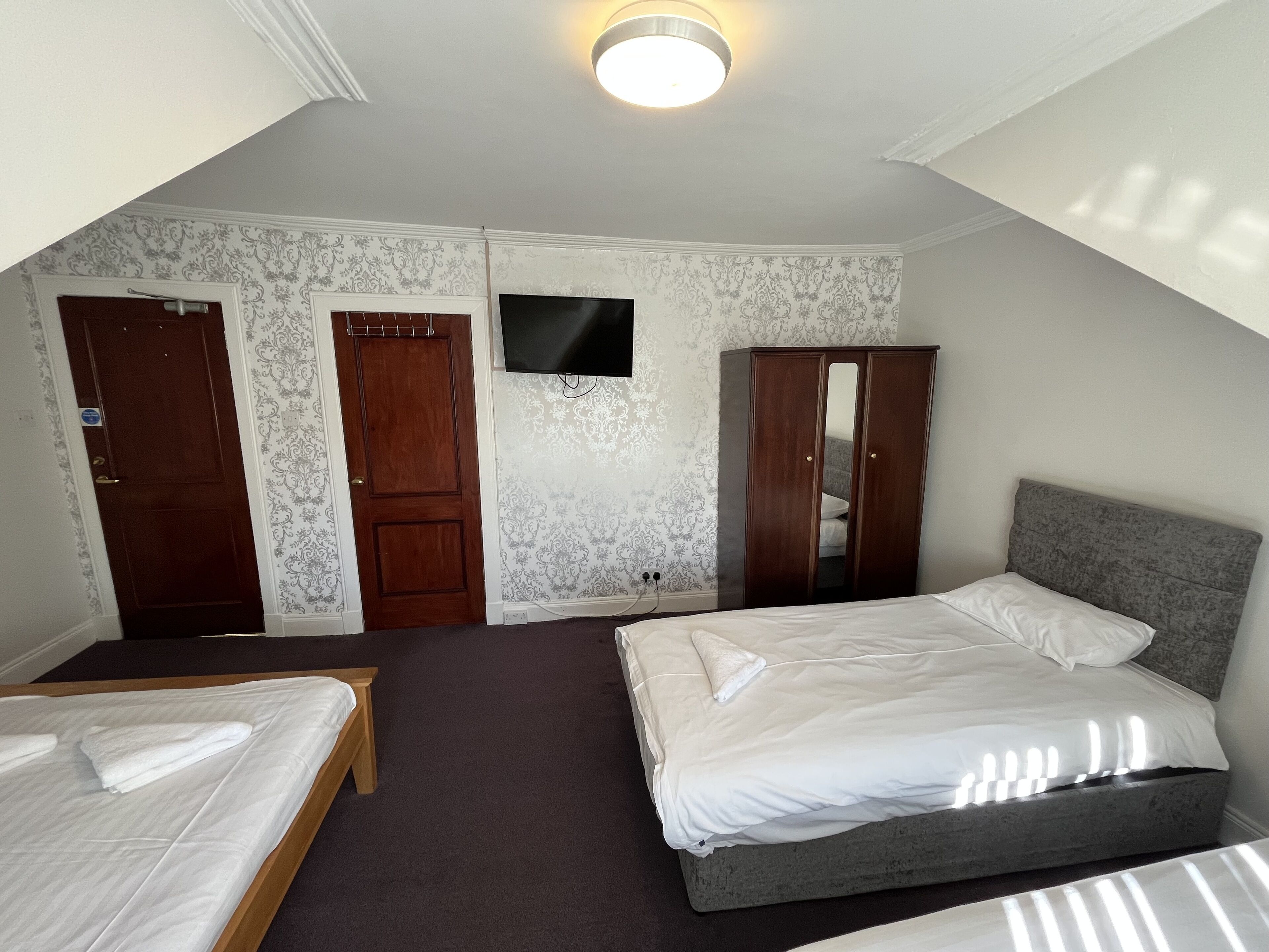 Een slaapkamer met twee bedden, een kledingkast, een televisie en behang met een patroon.