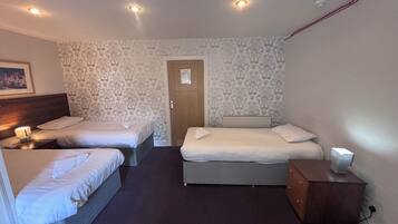 A hotel room with two single beds, a double bed, a wooden dresser, and a nightstand with a lamp.