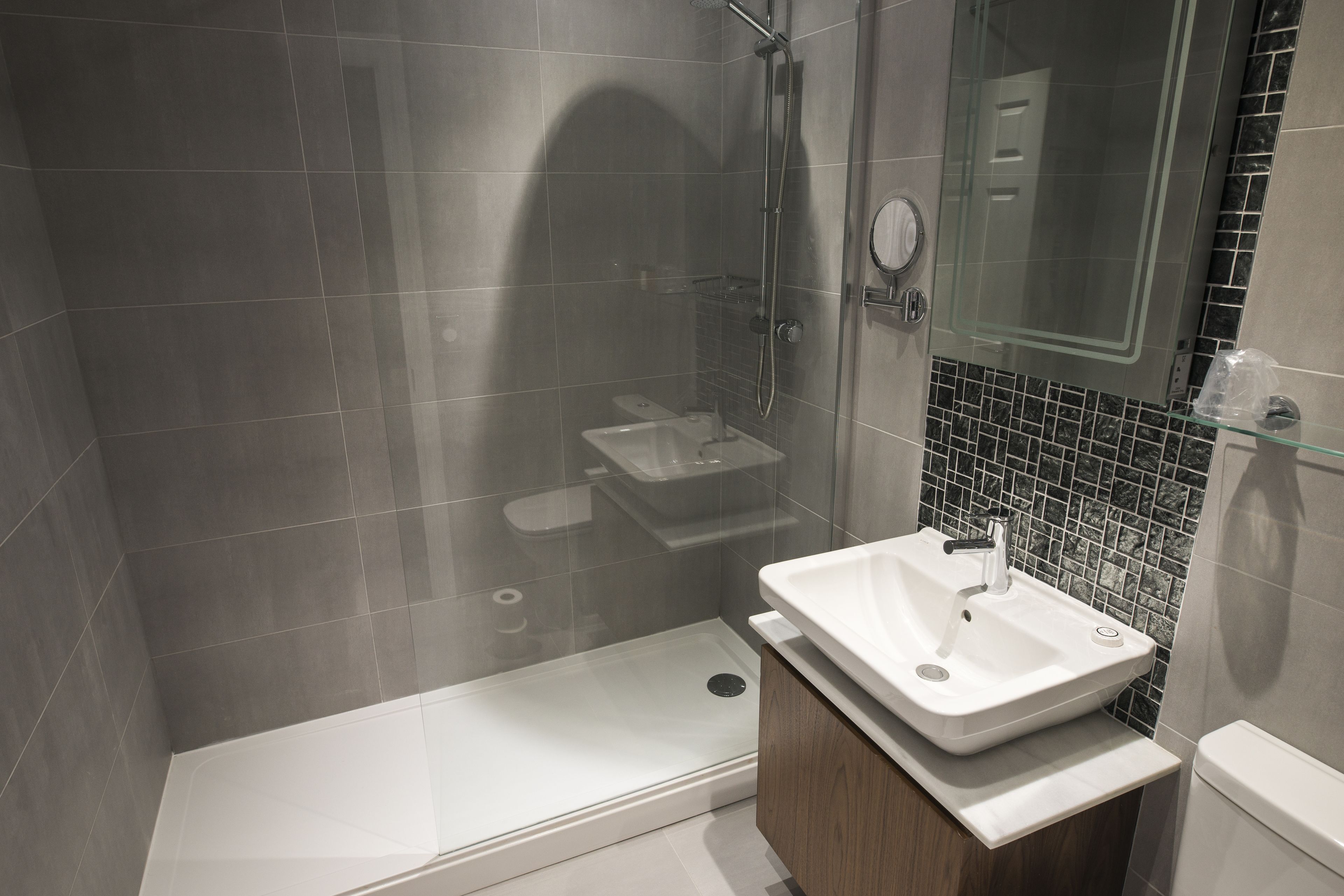 A modern bathroom with a glass-enclosed shower, a white sink, and a tiled backsplash.