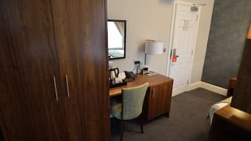 A hotel room with a wooden desk, a chair, a lamp, a telephone, and a wardrobe.