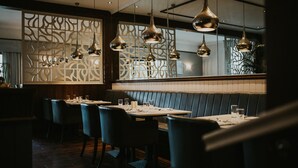 A restaurant with a modern interior, featuring a long dining table with chairs, pendant lighting, and a decorative partition wall. - The Croft Hotel (Darlington)