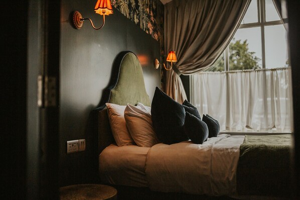 Una cama con cabecera, almohadas y una ventana con cortinas.