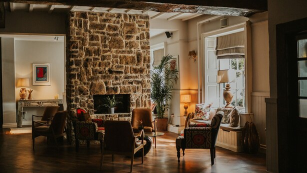 A cozy living room with a stone fireplace, comfortable seating, and a large window providing natural light. - The Croft Hotel (Darlington)