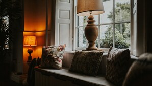 A window seat with a lamp, cushions, and a view of greenery outside. - The Croft Hotel (Darlington)