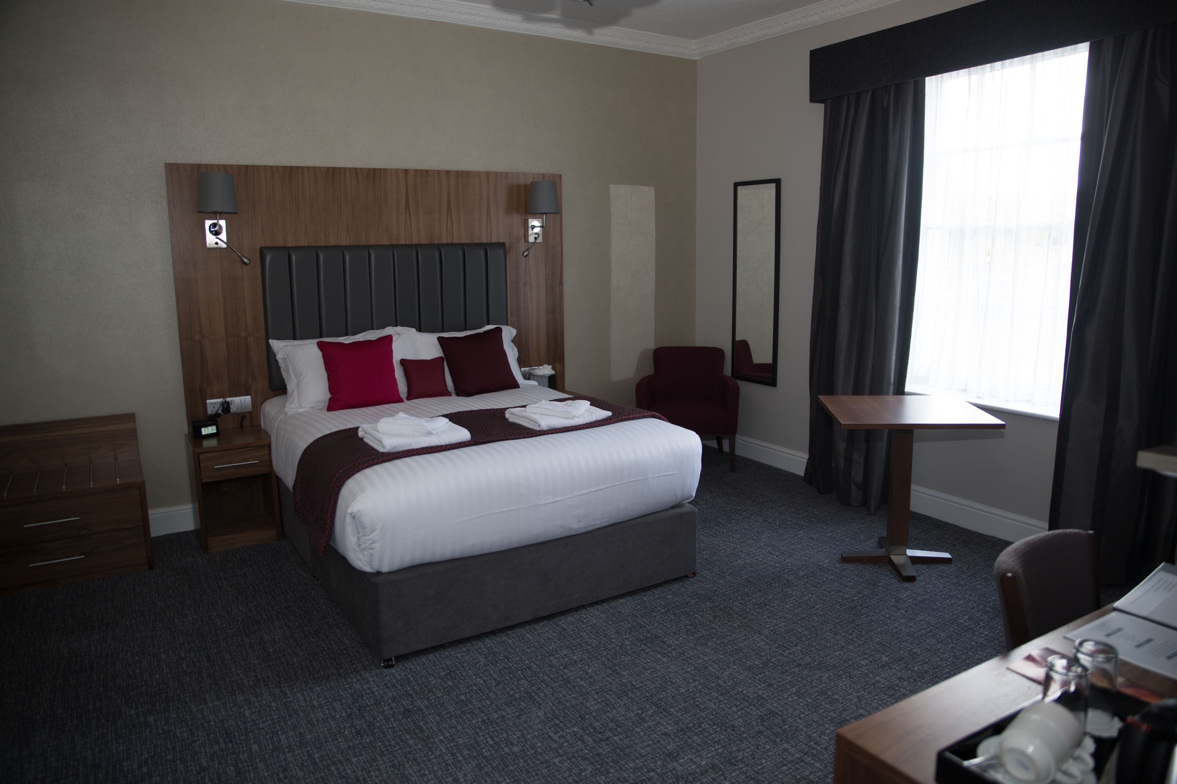 Habitación de hotel con una cama grande, un escritorio, una silla, una mesita y una ventana con cortinas.