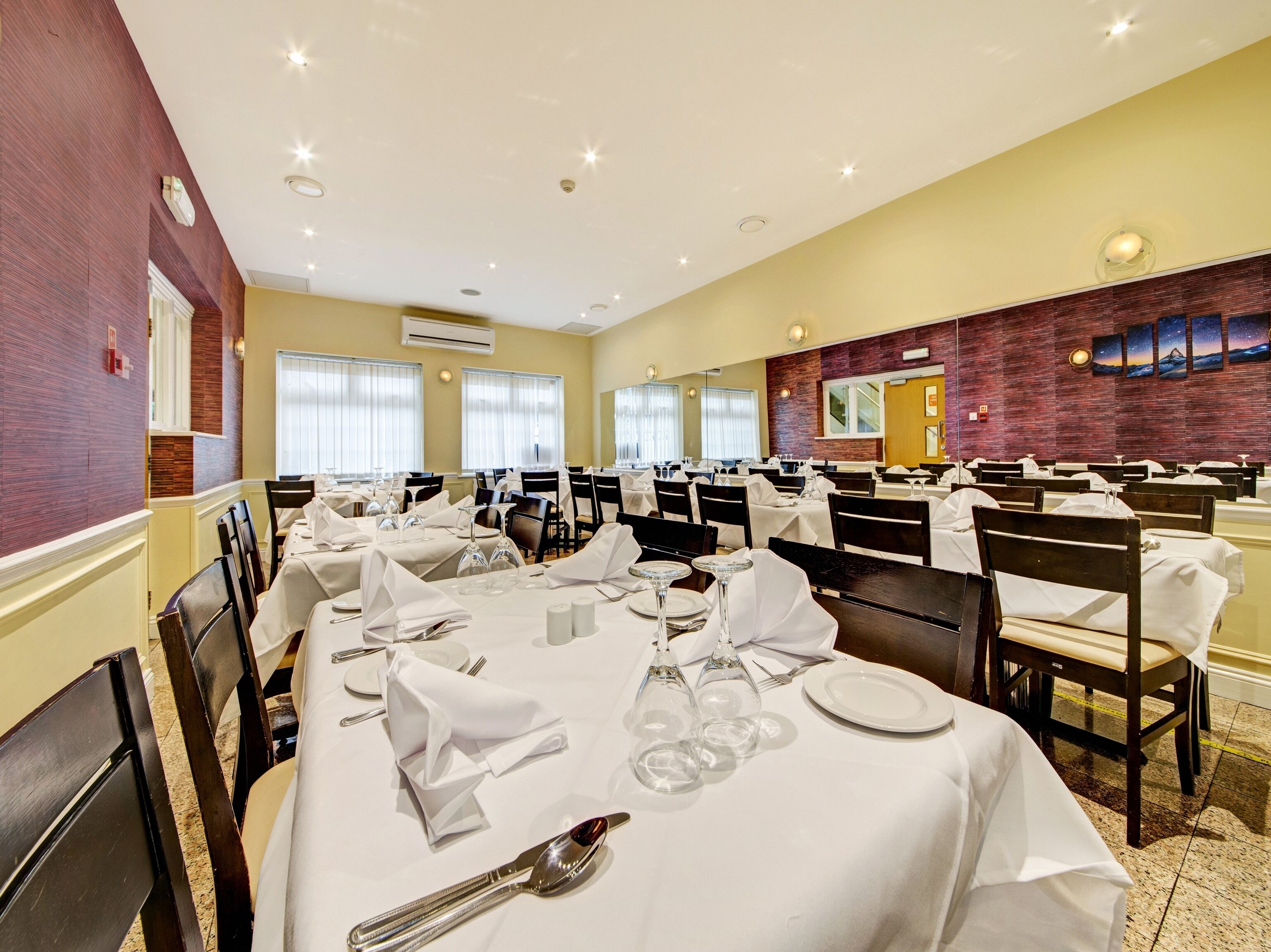 Une salle de banquet avec de nombreuses tables dressées pour le repas, agrémentées de nappes blanches, de couverts en argent et de verres.