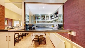A modern kitchen with a central island, bar area with shelves of bottles and glasses, and a dining area with chairs and tables. - OYO Bostons Manor Hotel, Hanwell London (London)
