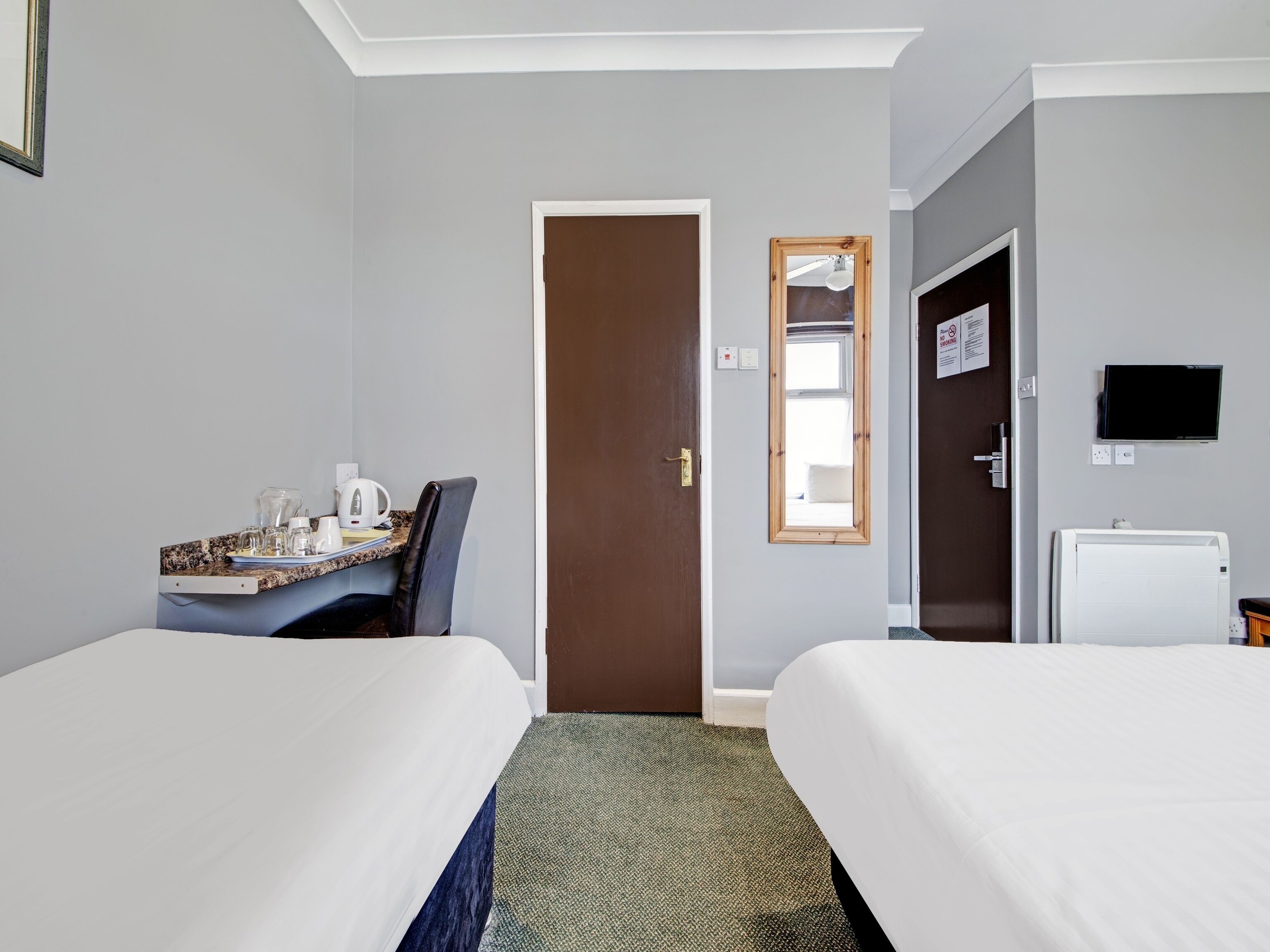 A hotel room with two beds, a desk with a chair, a television, and a small refrigerator.