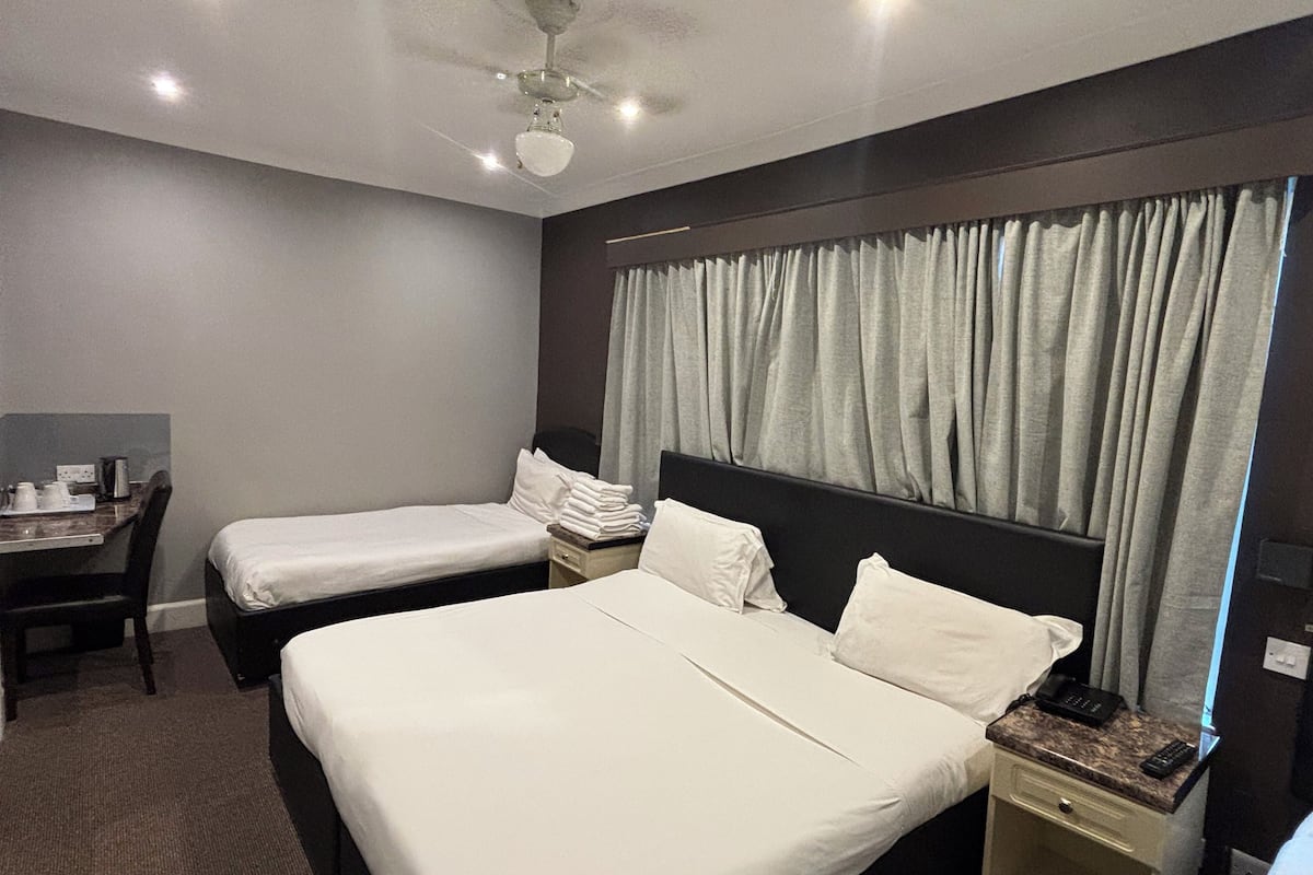 A hotel room with two single beds, a desk with a chair, a nightstand, and a ceiling fan.