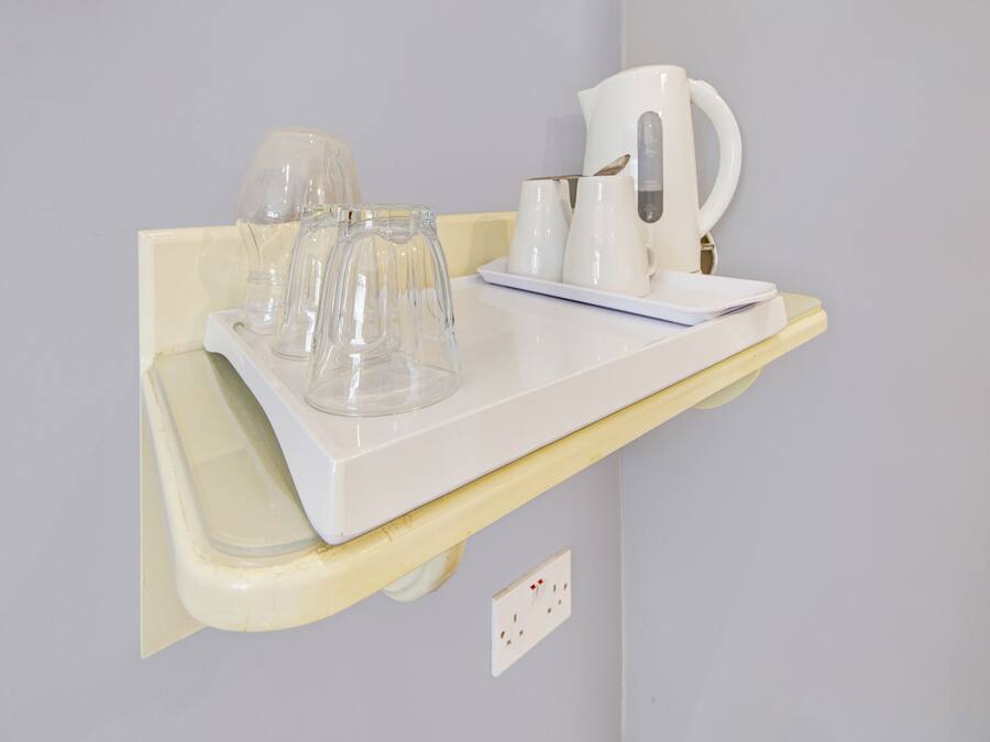 Un plan de travail blanc sur lequel se trouve un plateau contenant des verres en verre transparent et une bouilloire électrique blanche.