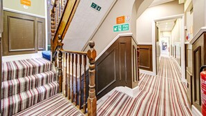 A hotel hallway with striped carpet, wooden banisters, and fire exit signs. - OYO Bostons Manor Hotel, Hanwell London (London)