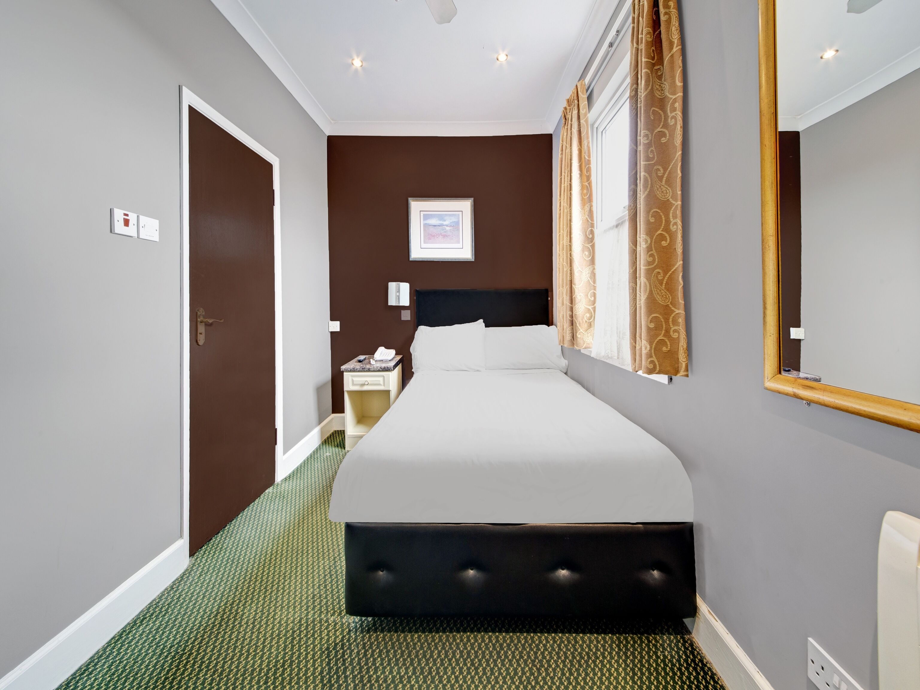 Hotelkamer met een groot bed, nachtkastje met telefoon, wandlamp en raam met gordijnen.