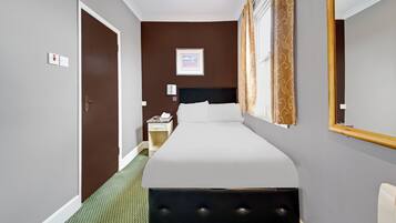Hotelkamer met een groot bed, nachtkastje met telefoon, wandlamp en raam met gordijnen.