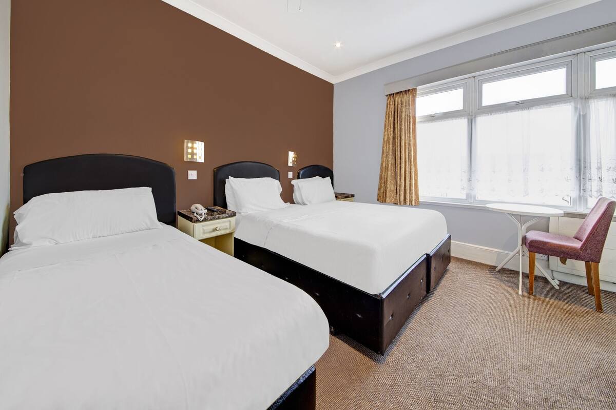 A hotel room with two beds, a desk, a chair, and a large window.