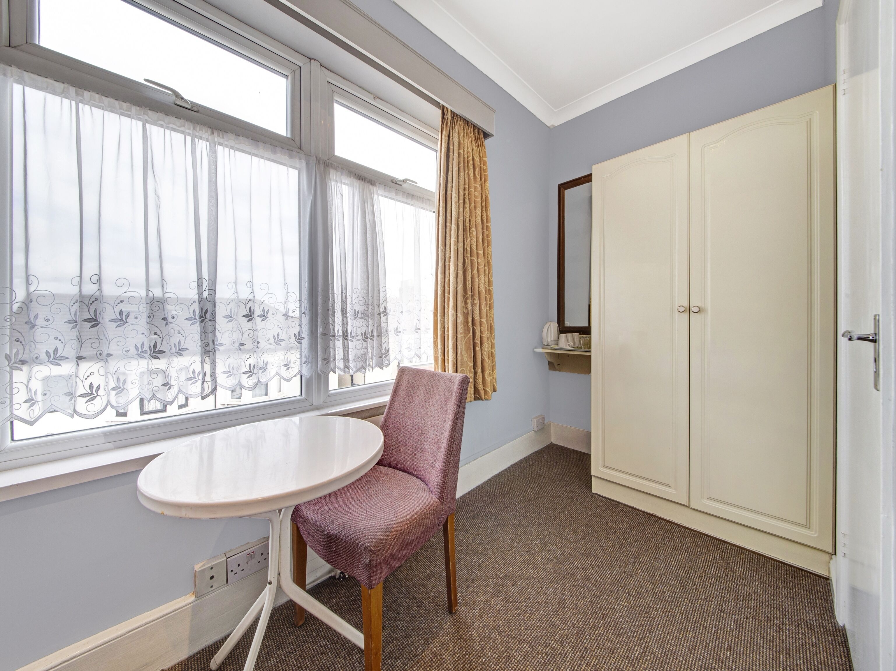 A hotel room with a round table, a chair, a wardrobe, and a window with curtains.