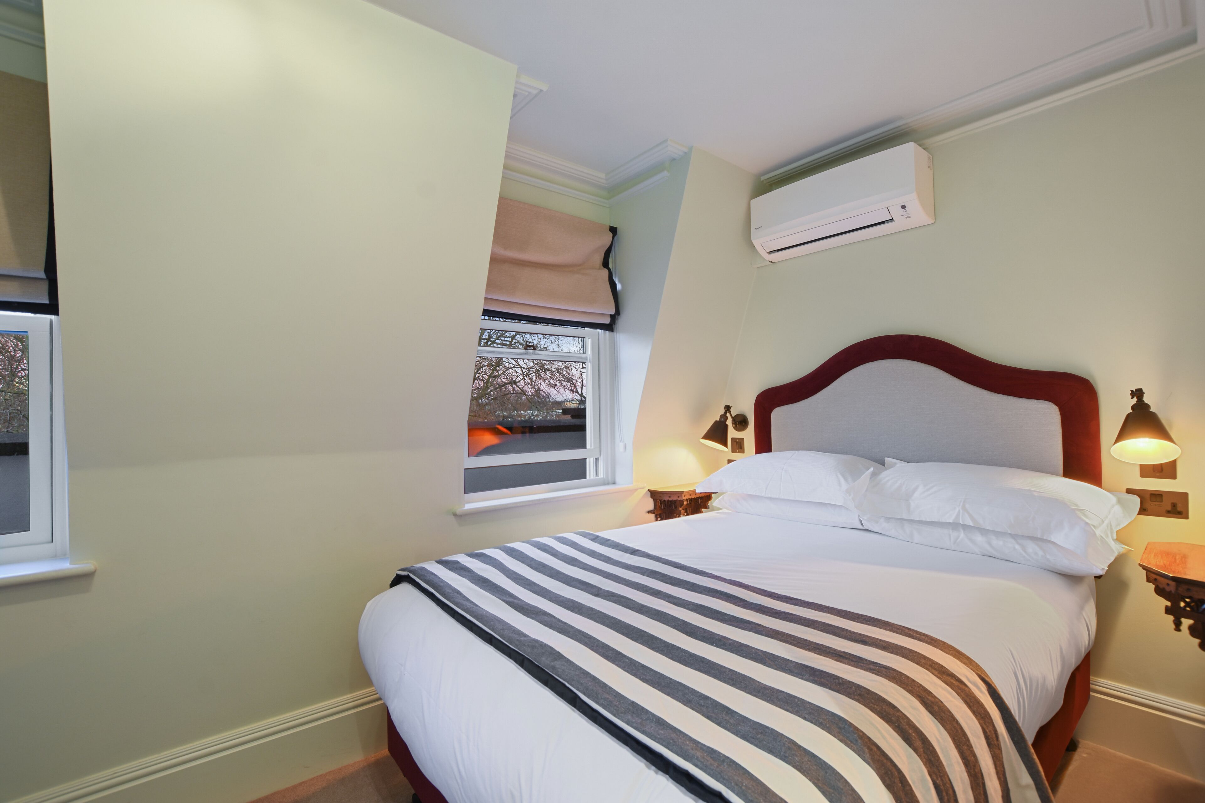 Un letto rifatto con una coperta a righe, una lampada da comodino e una finestra con vista sulla città.