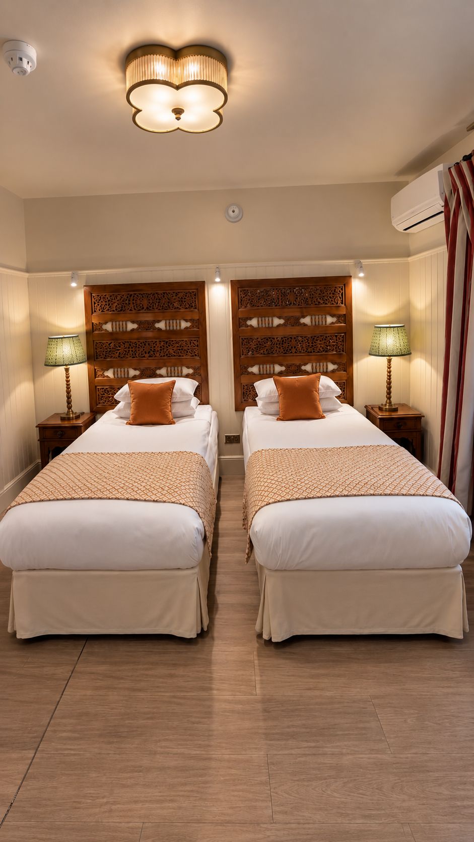 Une chambre d’hôtel avec deux lits, une tête de lit décorative, des lampes de chevet et un appareil de climatisation.