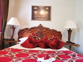 Una cama bien hecha con almohadas rojas, cabecera de madera, dos lámparas de noche y una obra de arte enmarcada en la pared.