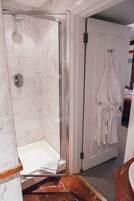 Ein Badezimmer mit einer gläsernen Duschkabine, einem weißen Bademantel, der an der Tür hängt, und einem Marmorboden.