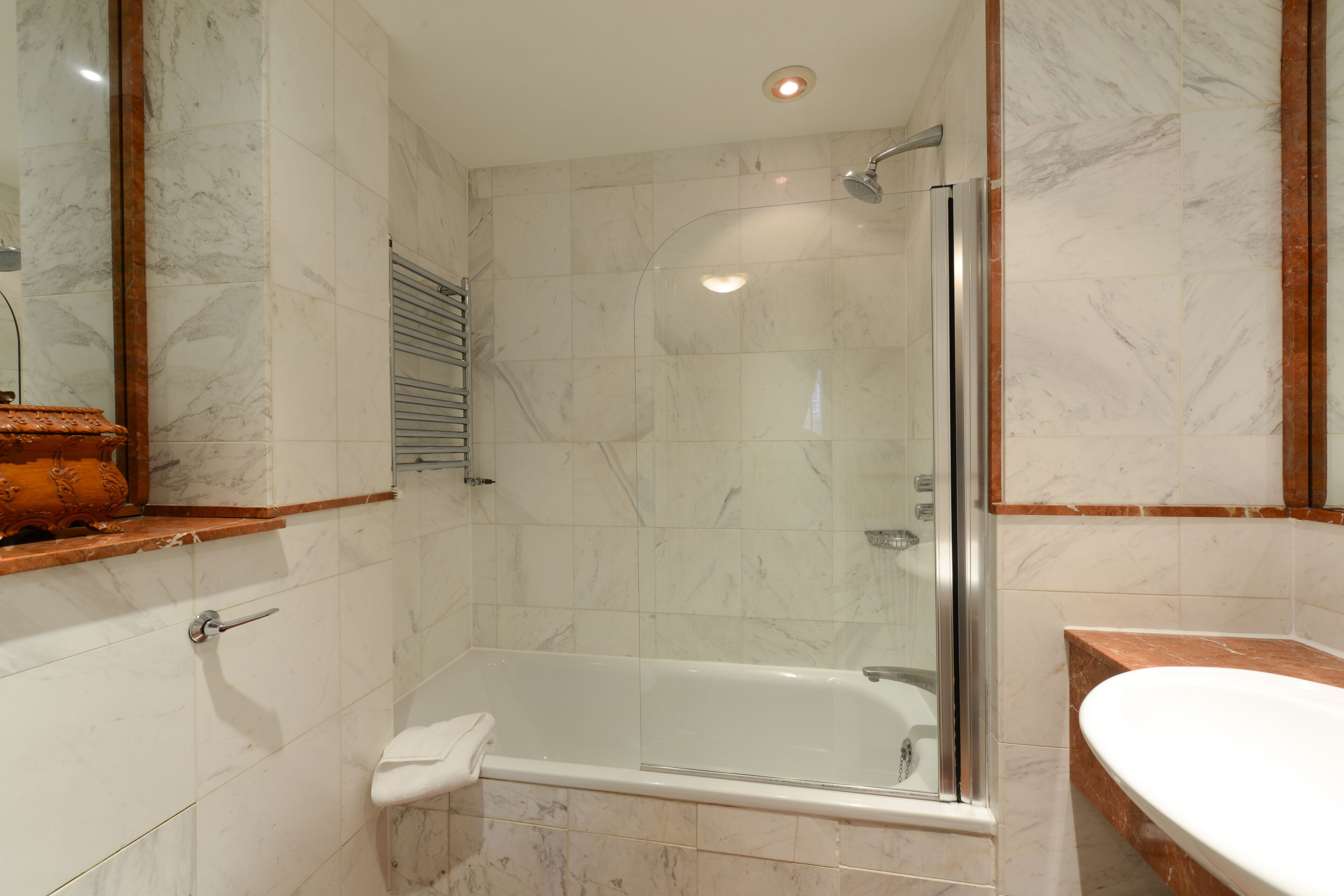A modern bathroom with a glass-enclosed shower, a bathtub, and a marble-tiled wall.