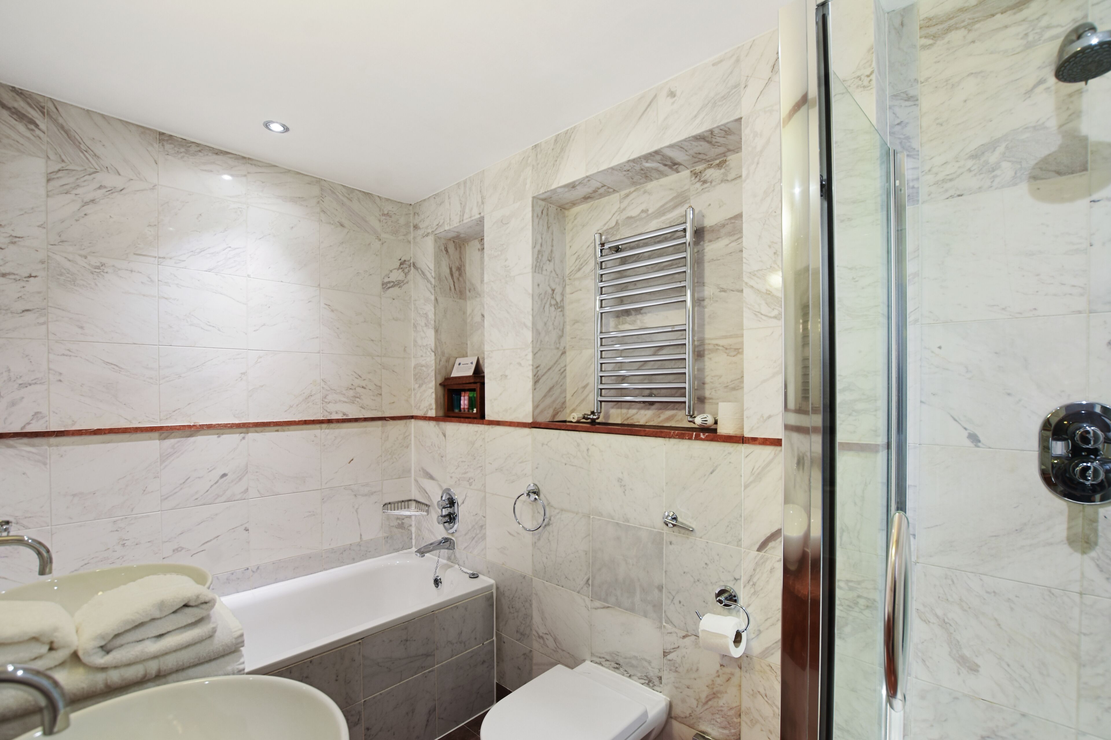 A modern bathroom with a bathtub, toilet, and glass shower enclosure.